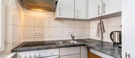 A modern kitchen with white cabinets, a stainless steel range hood, a double sink, and a built-in oven.