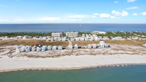Luchtbeeld van een kusthotelgebied met meerdere gebouwen, waarvan sommige balkons hebben, en een strand op de voorgrond.