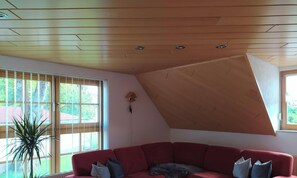 A living room with a red sofa, a potted plant, and a sloped ceiling.