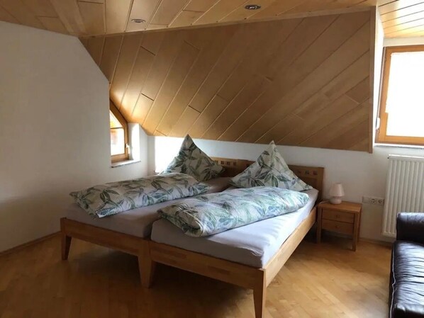 A bedroom with a sloped ceiling, a bed with floral bedding, a bedside table with a lamp, and a window.