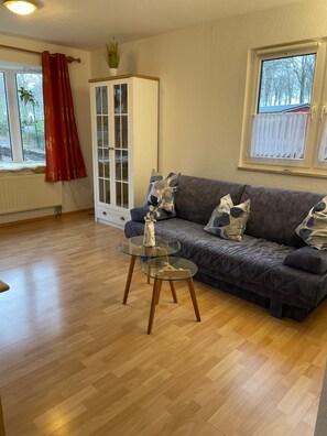 A living room with a sofa, a glass coffee table, a cabinet, and a window with curtains.