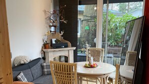 A room with a sofa, dining table, chairs, a TV, and a large window. - Holiday Home 'Strandhuette Dc We 46' with Private Terrace, Private Garden and Wi-Fi (Graal- Müritz)