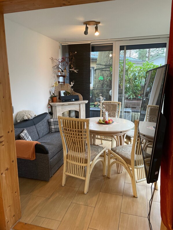 A room with a sofa, dining table, chairs, a TV, and a large window.