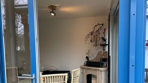 A room with a glass door, a white table, two wicker chairs, a fireplace, and a ceiling fan. - Holiday Home 'Strandhuette Dc We 46' with Private Terrace, Private Garden and Wi-Fi (Graal- Müritz)