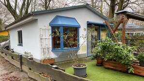 A small, single-story house with a blue front door and windows, surrounded by a wooden fence and potted plants. - Holiday Home 'Strandhuette Dc We 46' with Private Terrace, Private Garden and Wi-Fi (Graal- Müritz)