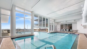 Une piscine intérieure dotée de grandes fenêtres, d’un espace aménagé au bord du bassin et offrant une vue sur l’extérieur.