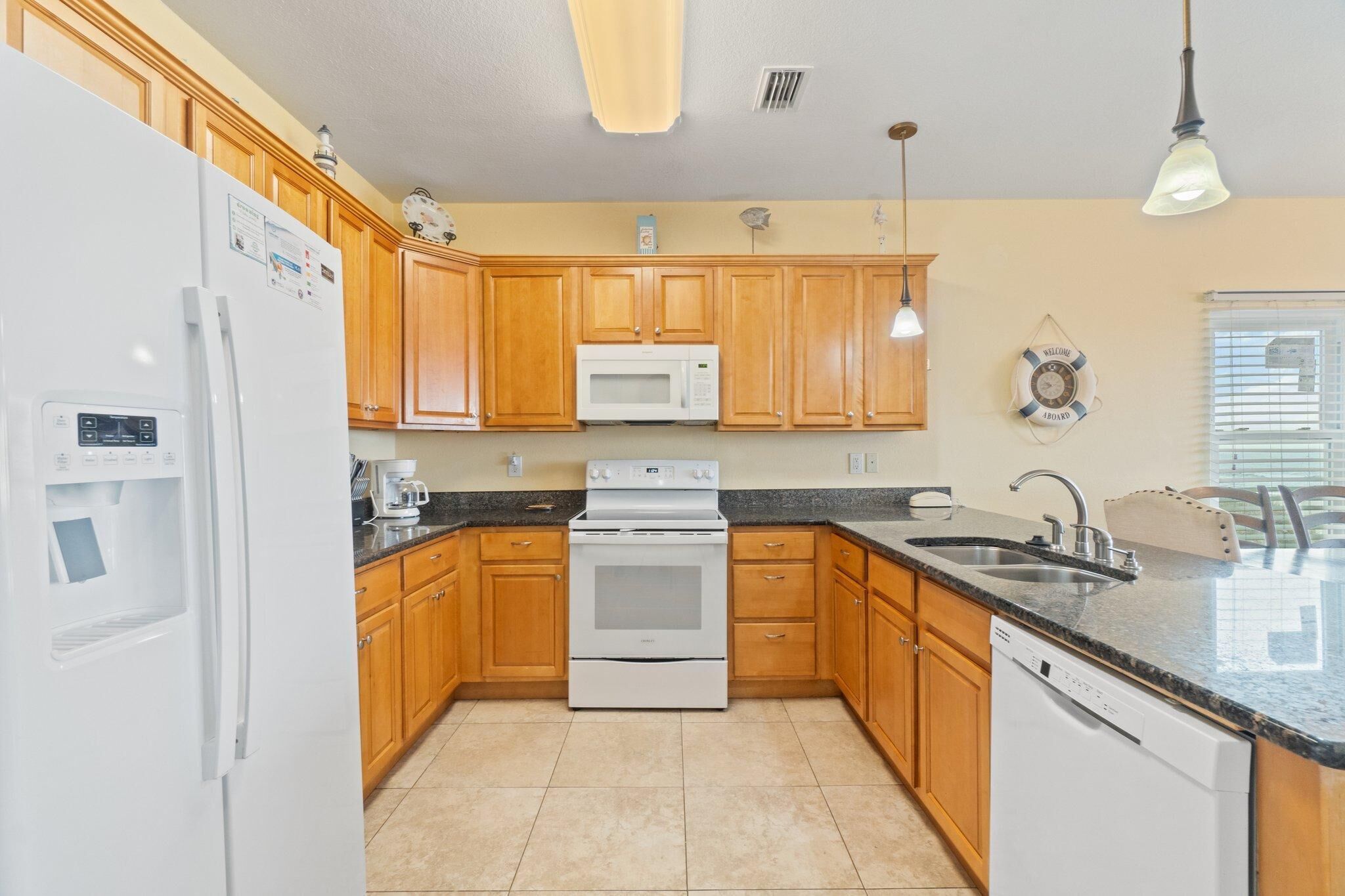 A kitchen with wooden cabinets, a white refrigerator, a microwave, a stove, a dishwasher, and a sink.
