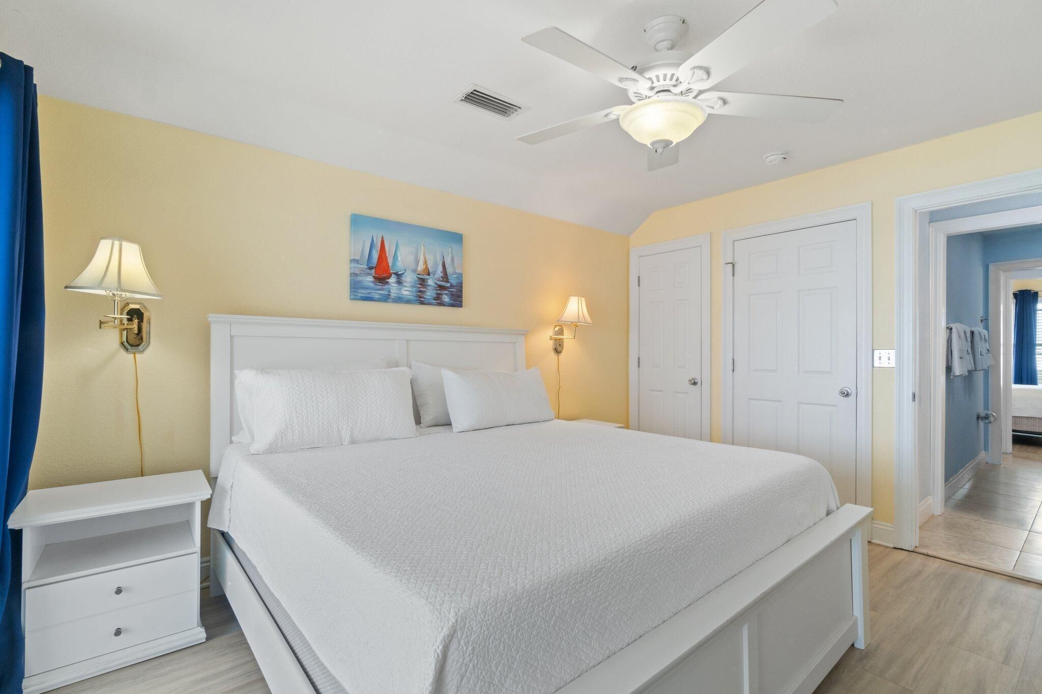 A bedroom with a bed, nightstands, a ceiling fan, and a painting on the wall.