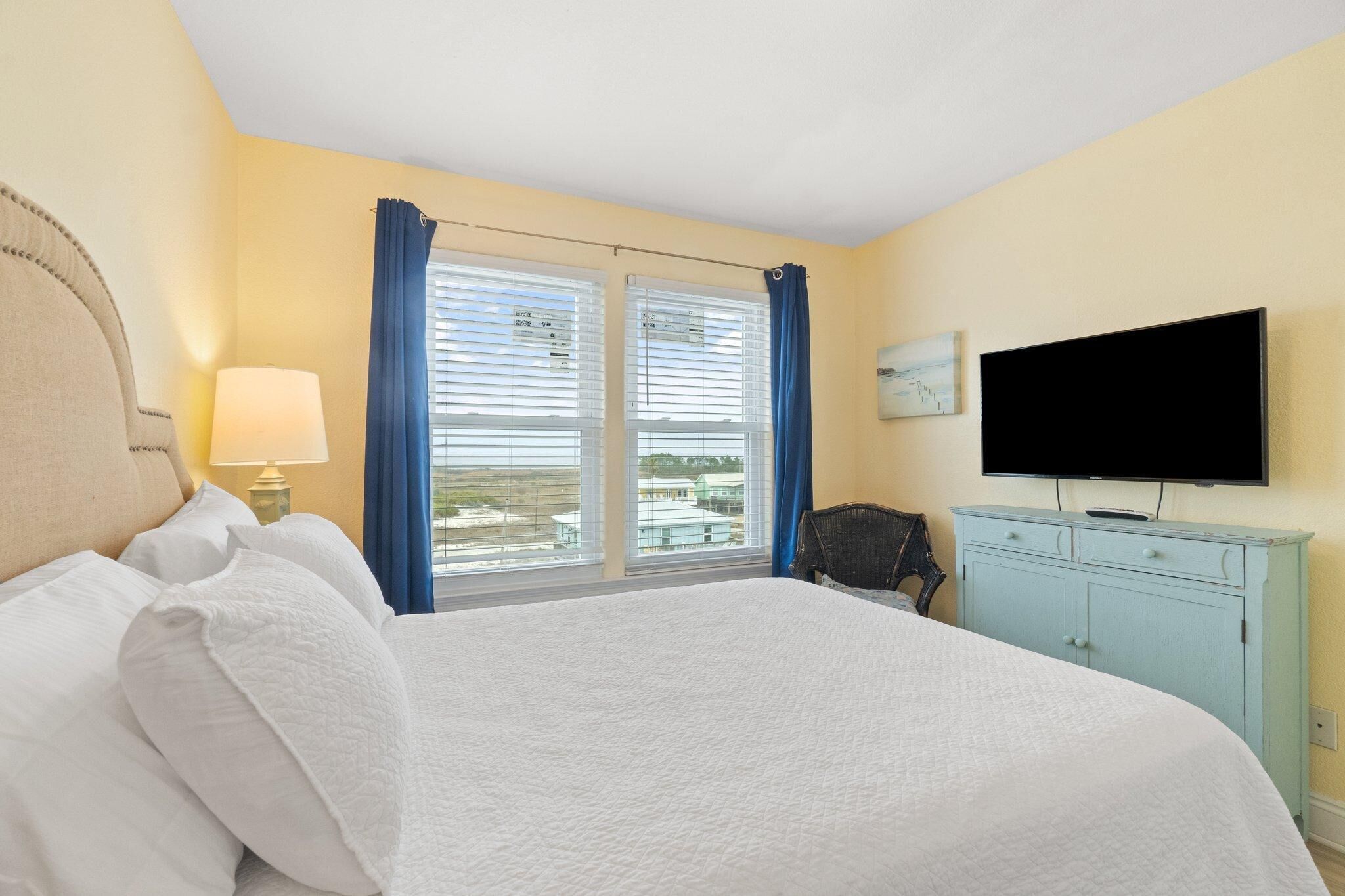 A hotel room with a bed, a television, a desk, and a window with curtains.