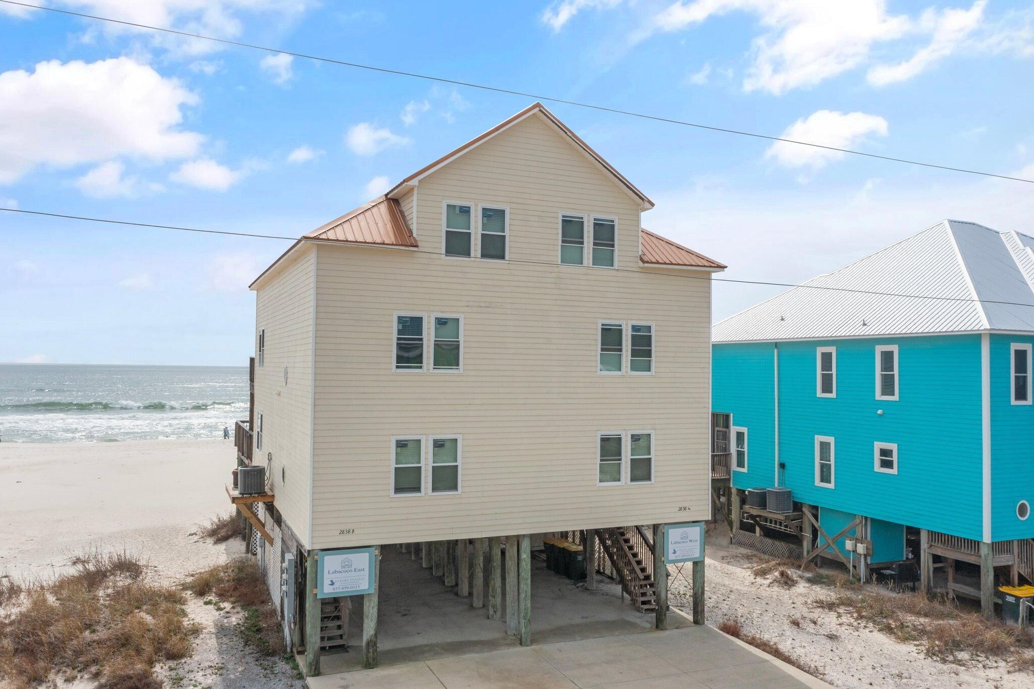 A two-story building with a flat roof, located on stilts near a beach.