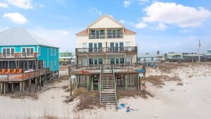 A multi-story beachfront building with a wooden deck and a staircase leading to the upper level. - Labacoco East (Gulf Shores)