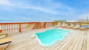 Une terrasse en bois avec une piscine, des chaises longues et une vue sur la plage et l’océan.