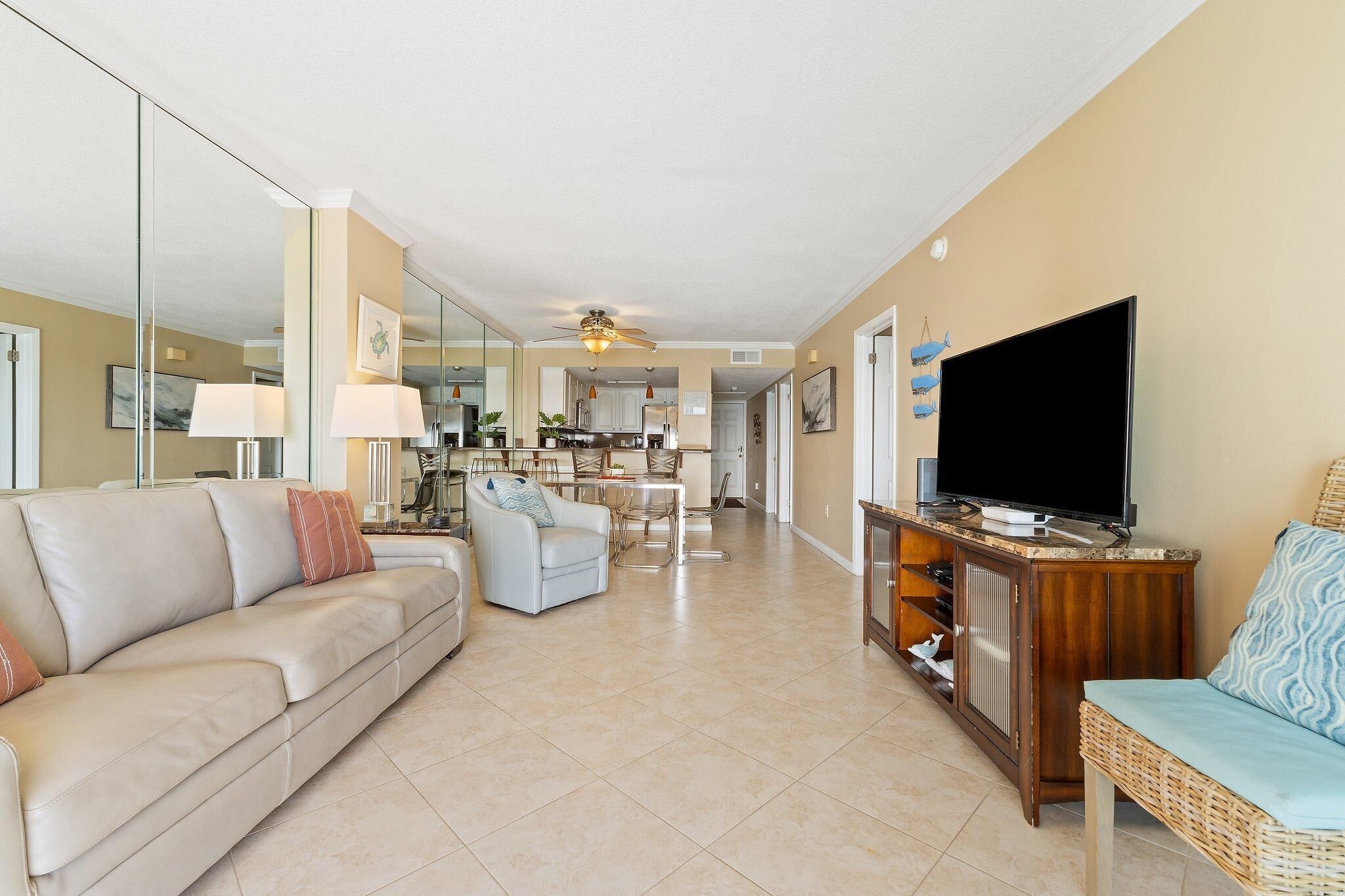 A spacious living room with a sofa, a television, and a dining area in the background.