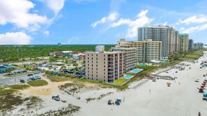 Un complejo turístico costero con varios edificios altos, un estacionamiento y una playa con sombrillas.