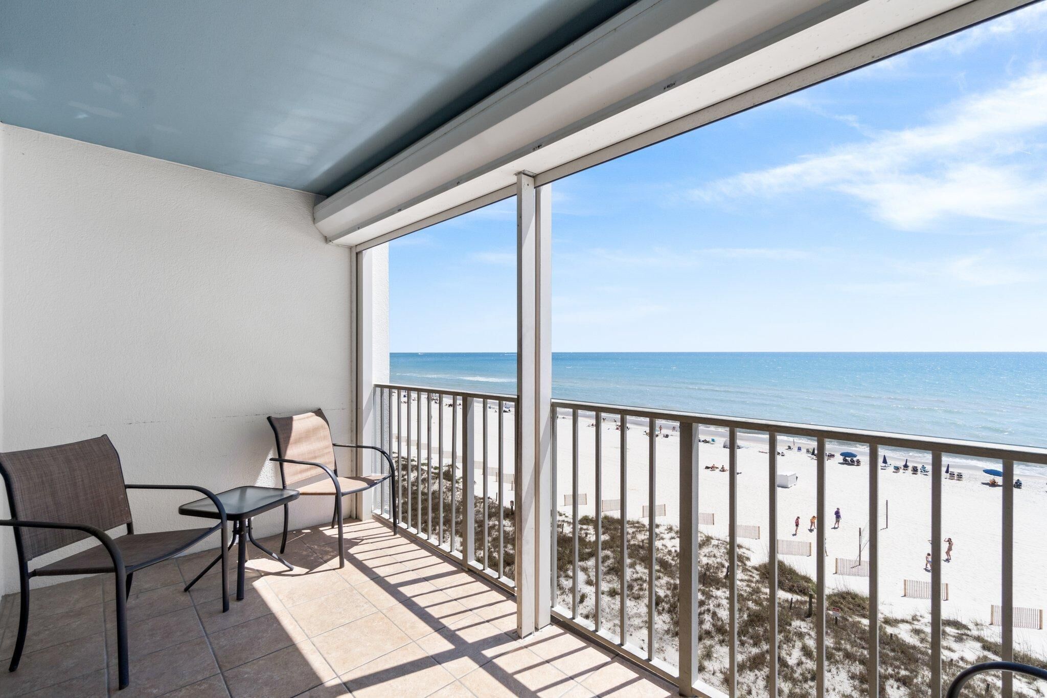 A balcony with a view of the beach, a table, and two chairs.
