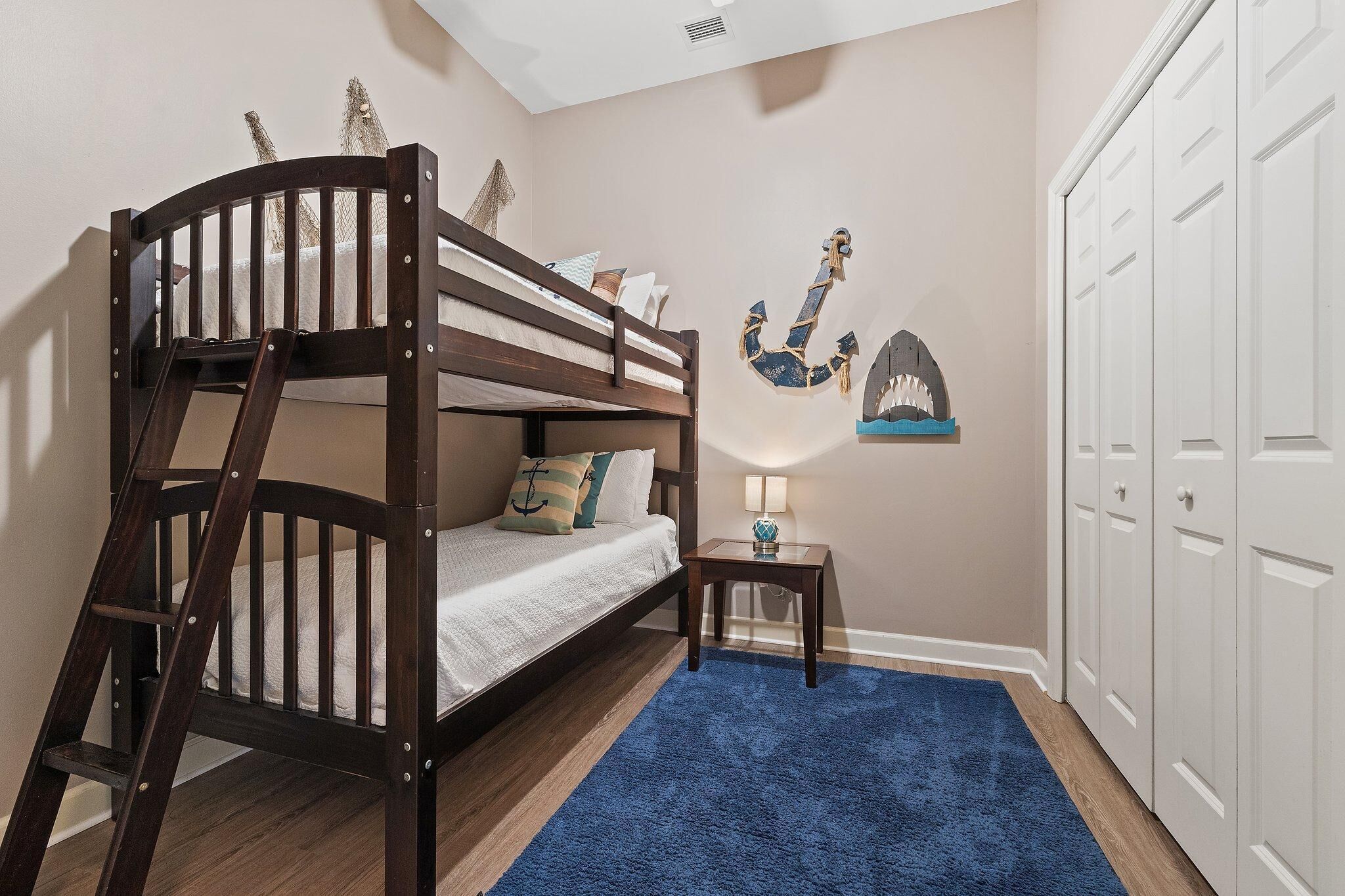 A bunk bed room with a ladder, a small table with a lamp, and nautical-themed wall decorations.