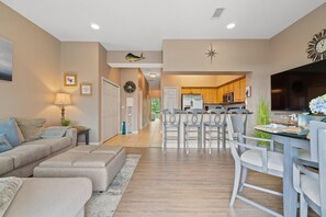 A modern living room with a sofa, ottoman, and a dining area with chairs and a table. - Villagio C246 (Pensacola)