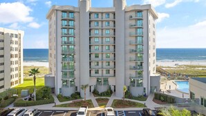 A multi-story hotel with balconies, a pool, and a beach view.