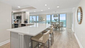 A modern kitchen with a large island, a dining area with a view, and a living space with a large window overlooking the ocean.