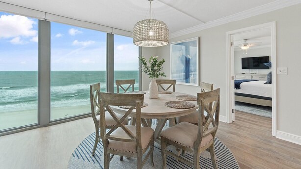 A dining area with a view of the ocean, a ceiling fan, and a bed in the adjacent room.