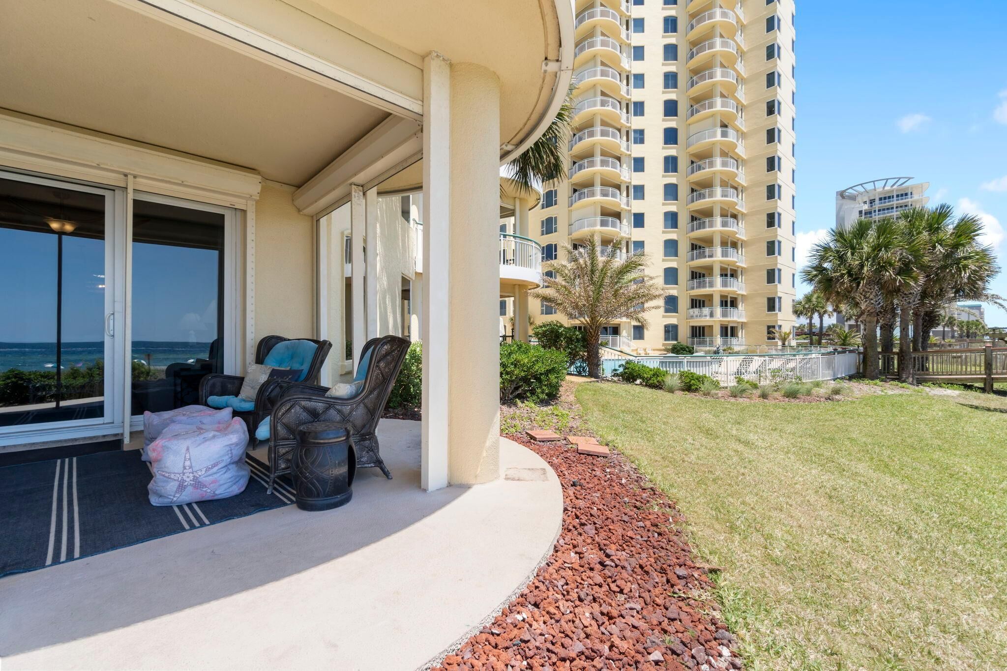 A balcony with outdoor furniture, a view of the ocean, and a tall building in the background.