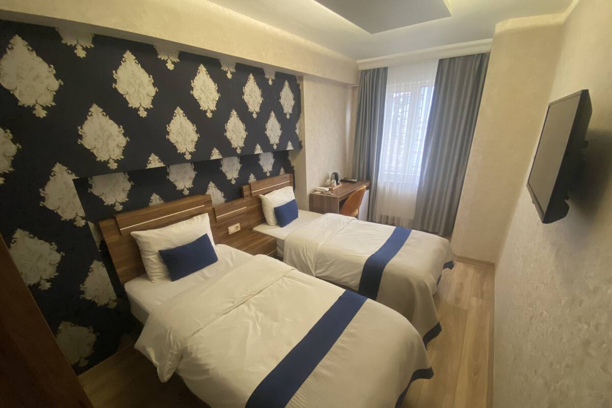 Une chambre d’hôtel avec deux lits, un bureau, une chaise, une télévision et une fenêtre avec des rideaux.