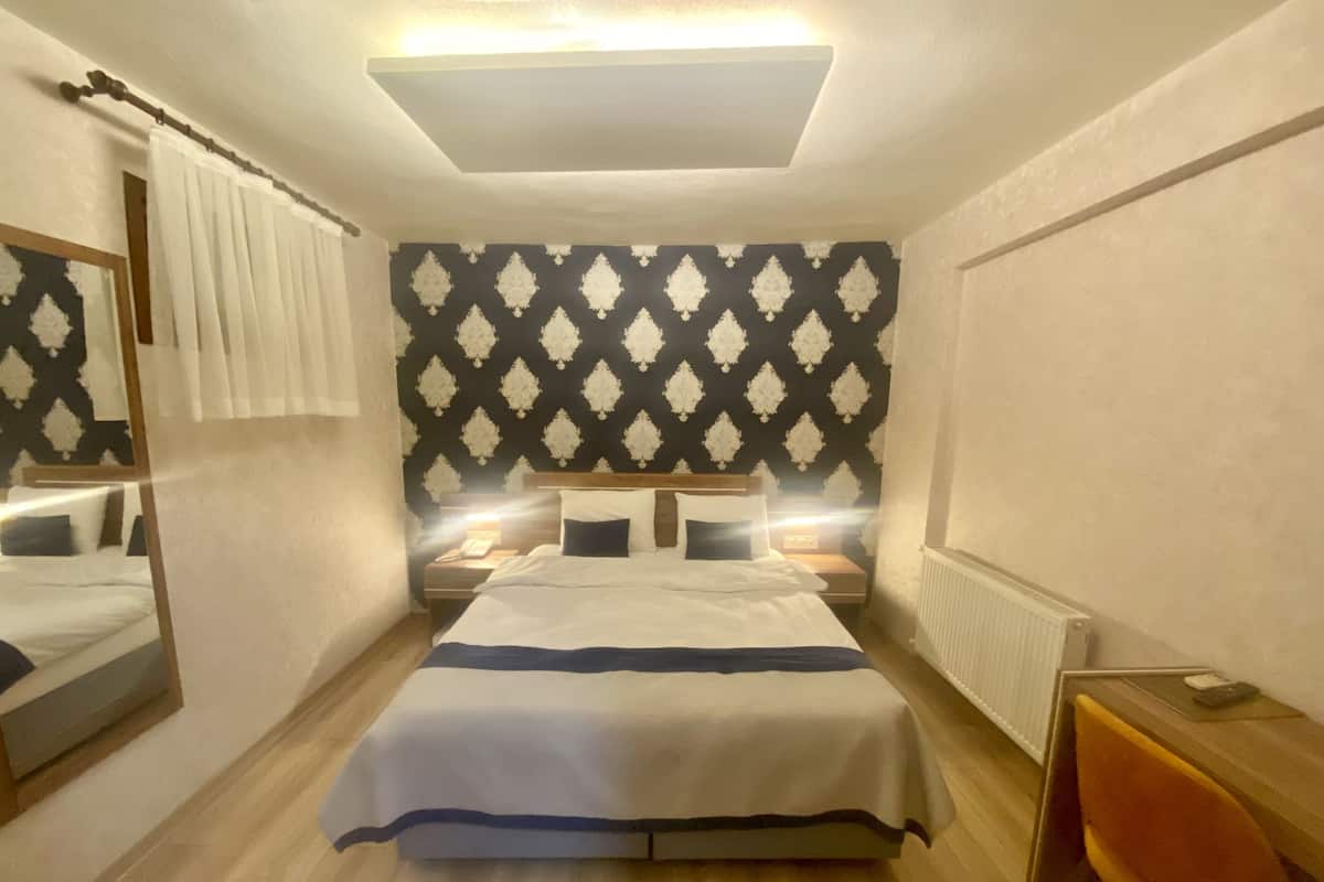 Une chambre d’hôtel avec un grand lit, des tables de chevet, un miroir et un radiateur.