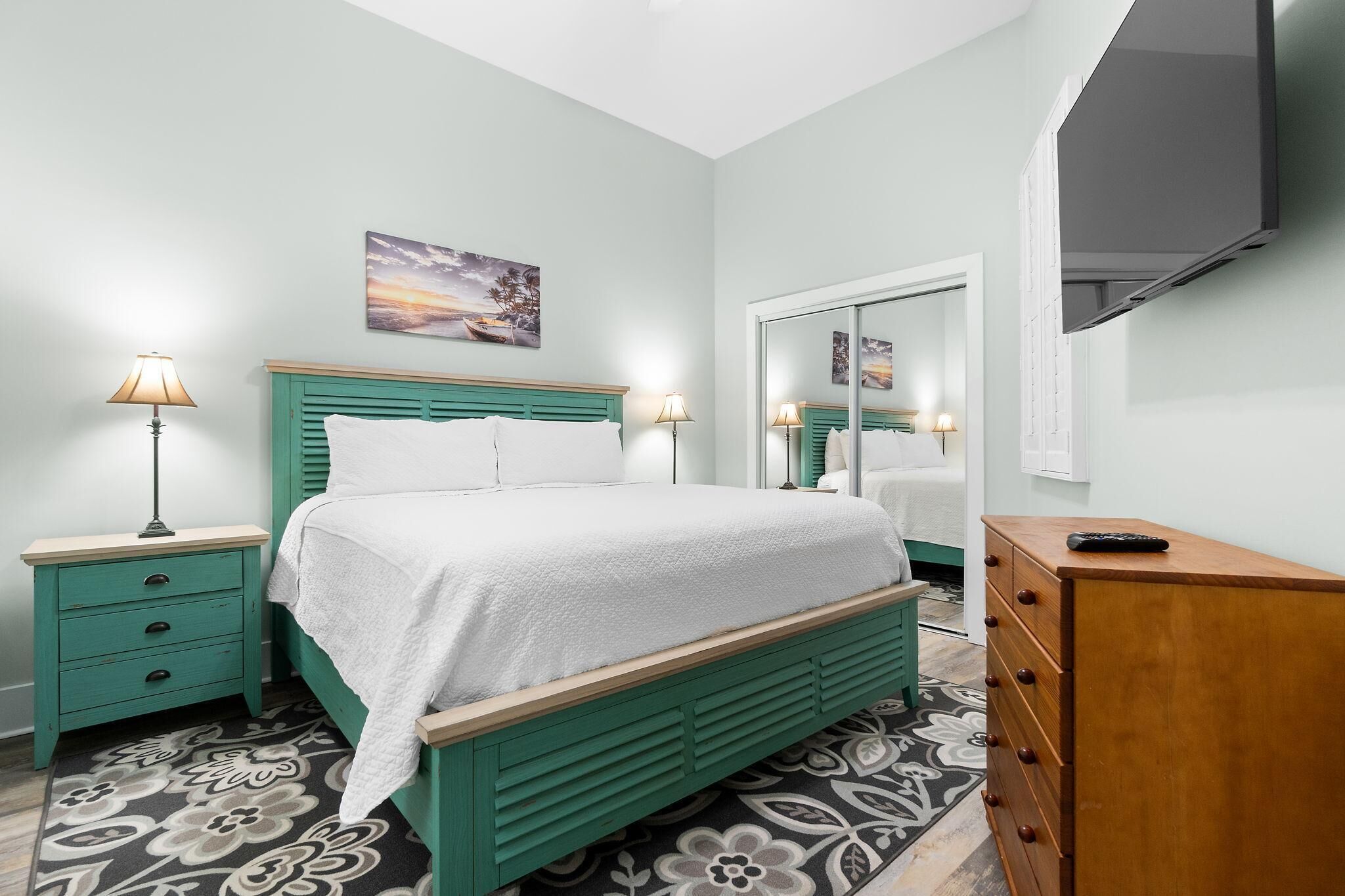 Une chambre à coucher comprenant un lit, des tables de chevet, une commode, un miroir et un téléviseur.