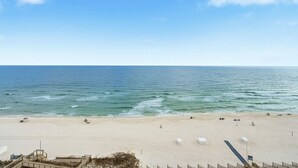 A beach with a clear sky, calm sea, and a sandy shore with a lifeguard tower and beach chairs. - Palacio 801 (Pensacola)