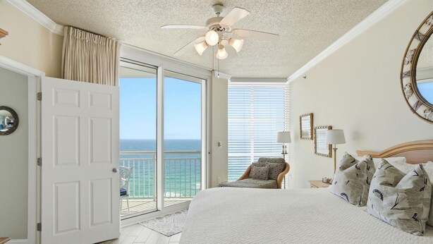 A bedroom with a large bed, a ceiling fan, a view to the ocean, and a door leading to a balcony. - Palacio 801 (Pensacola)