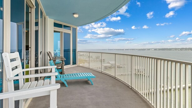 A balcony with chairs and a table, overlooking a body of water and distant buildings.