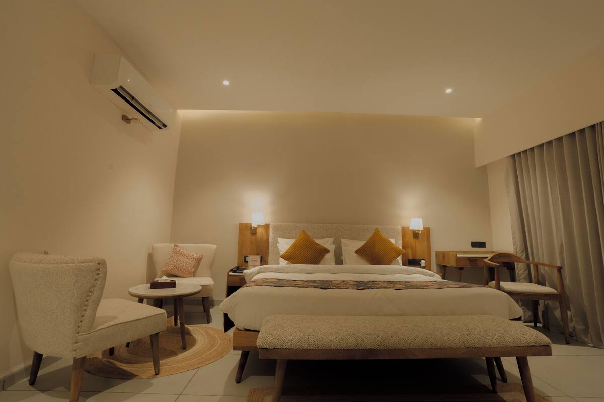 A hotel room with a large bed, bedside tables, a chair, a desk, and a lamp.