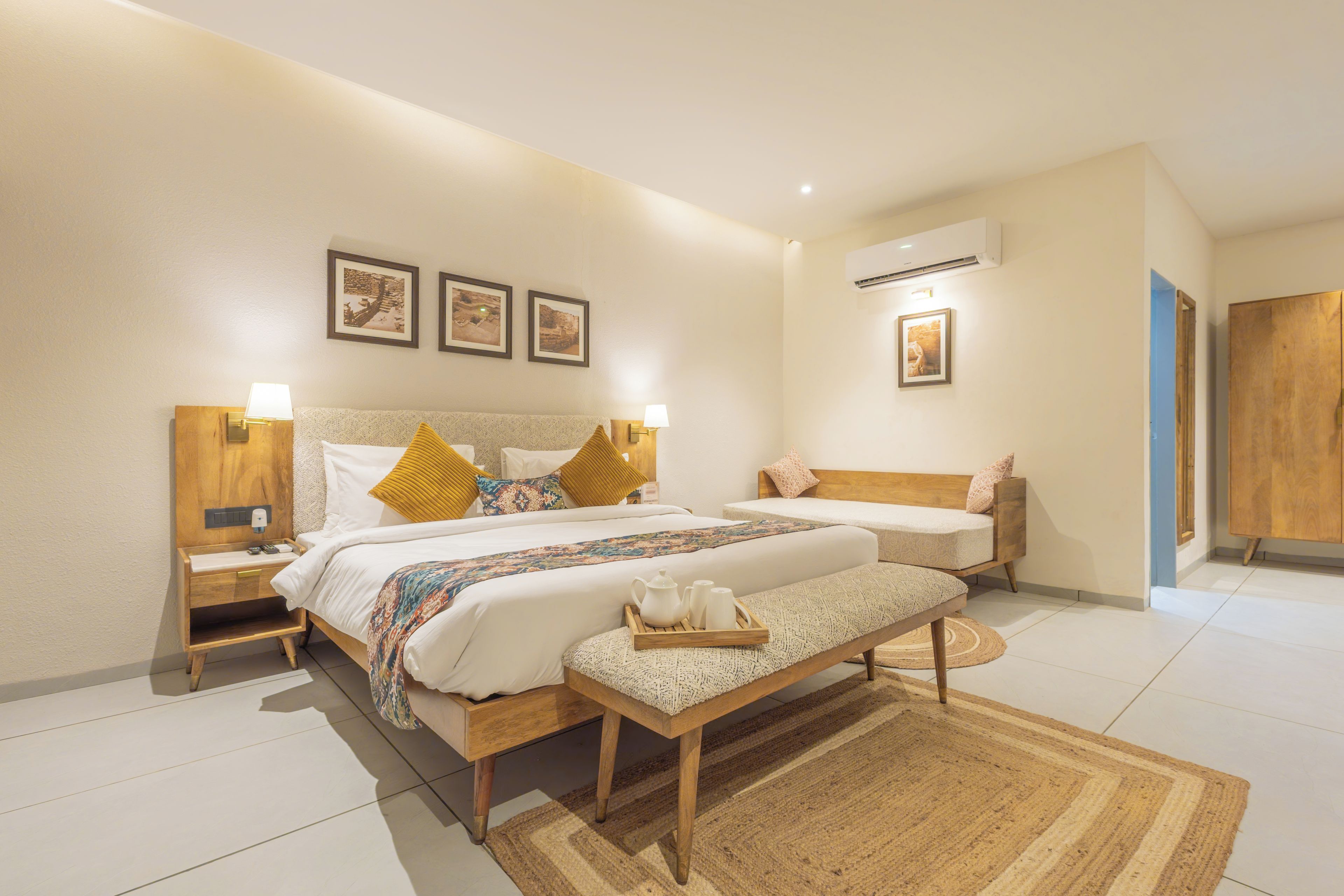 A hotel room with two beds, a wooden bench, a tray with toiletries, and a large window.