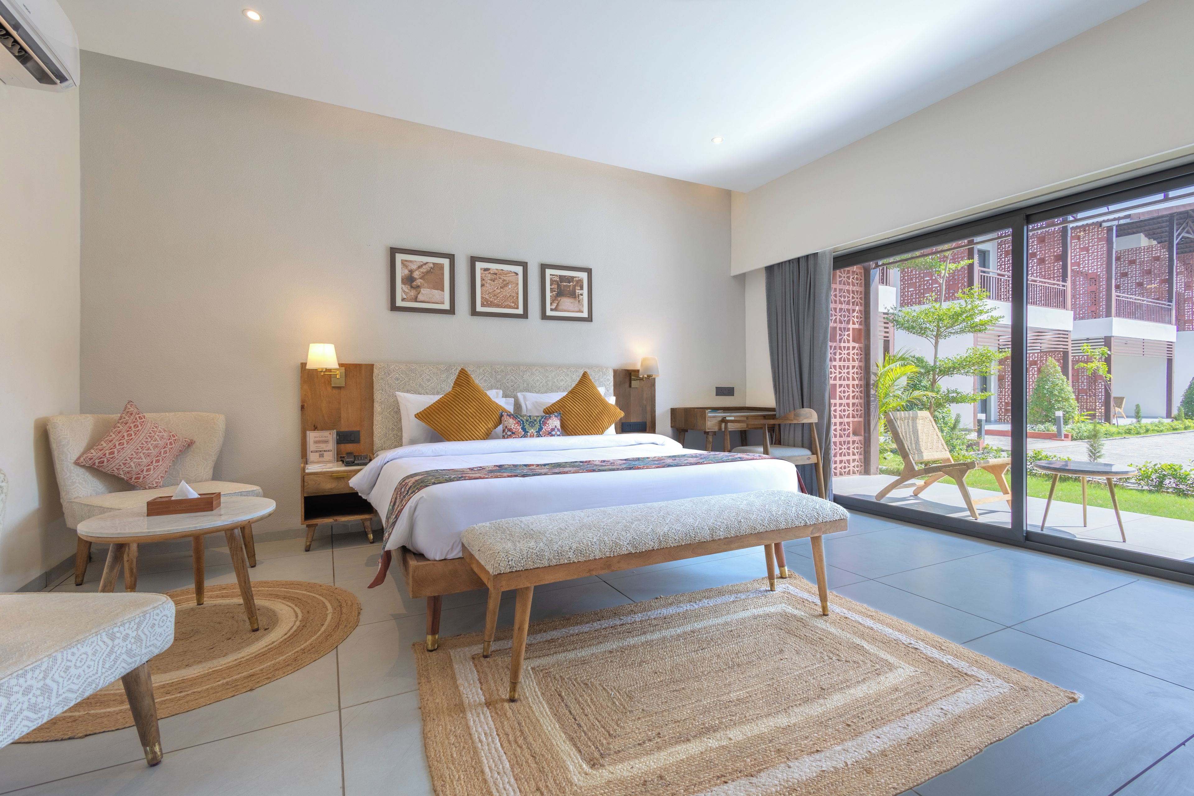A hotel room with a bed, bedside tables, a bench, a chair, and a view of the outside.