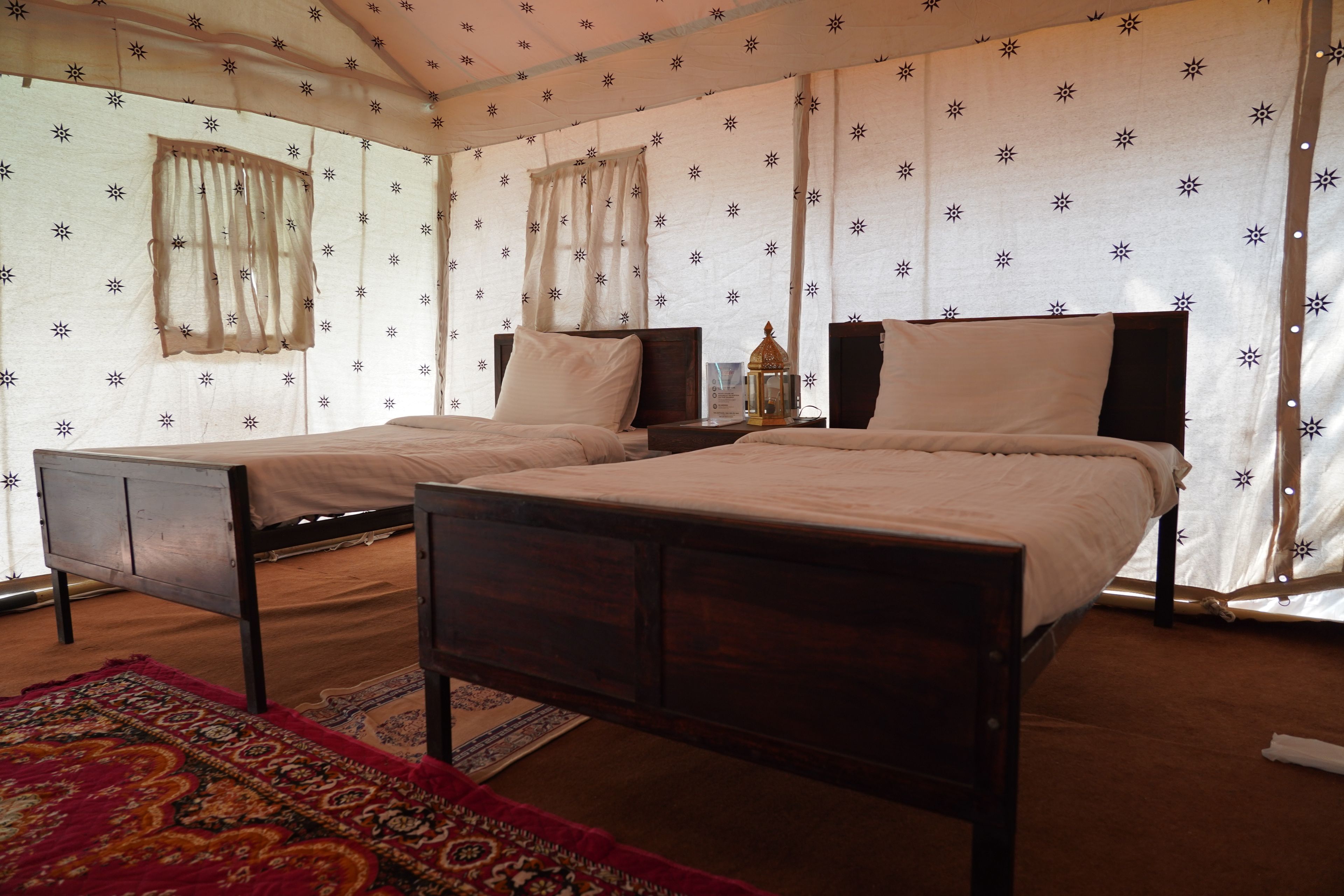 Ein Zimmer mit zwei Betten, einem Nachttisch, einer Lampe und einem gemusterten Teppich.