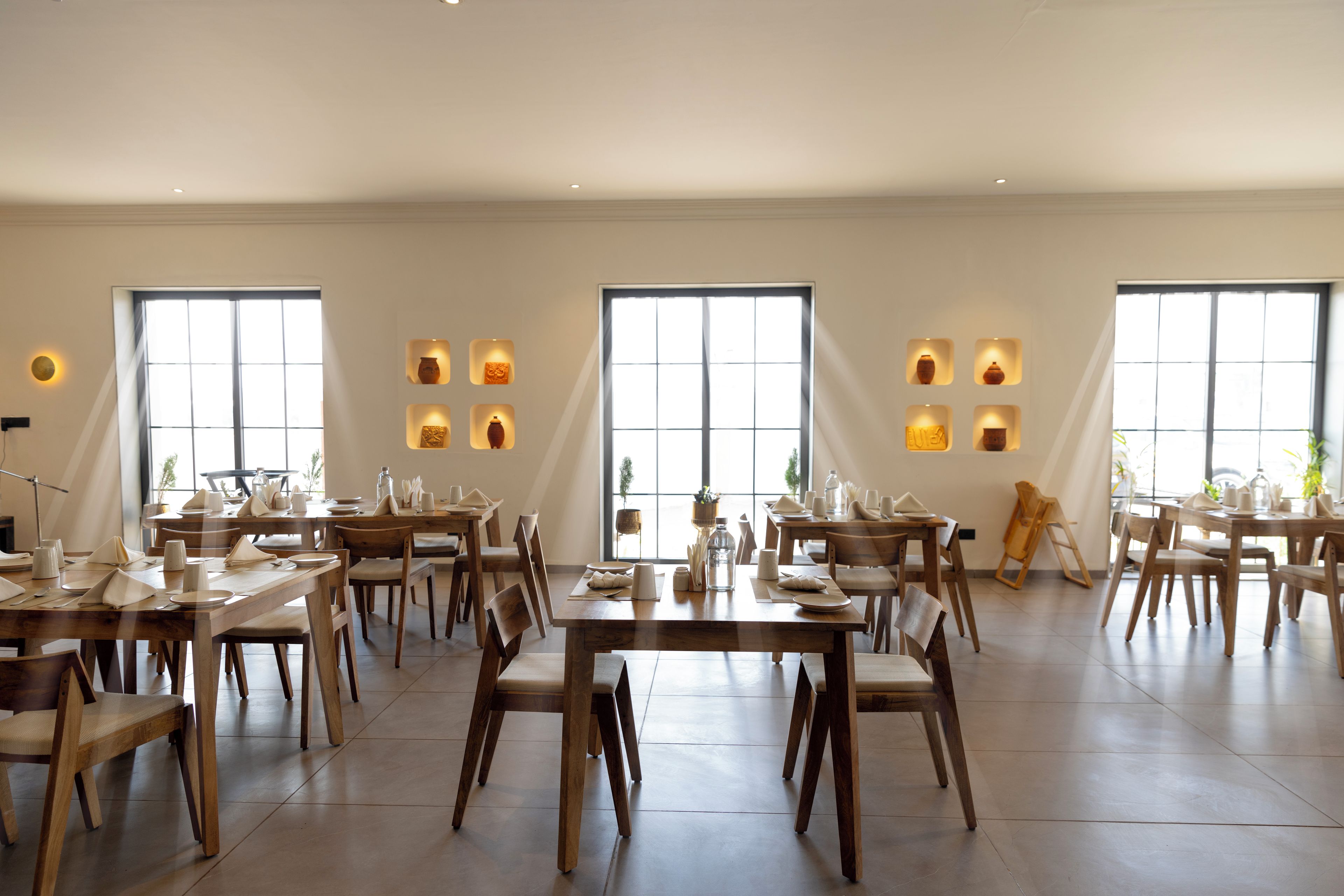Un'ampia sala da pranzo con diversi tavoli e sedie, grandi finestre e lampade a parete.