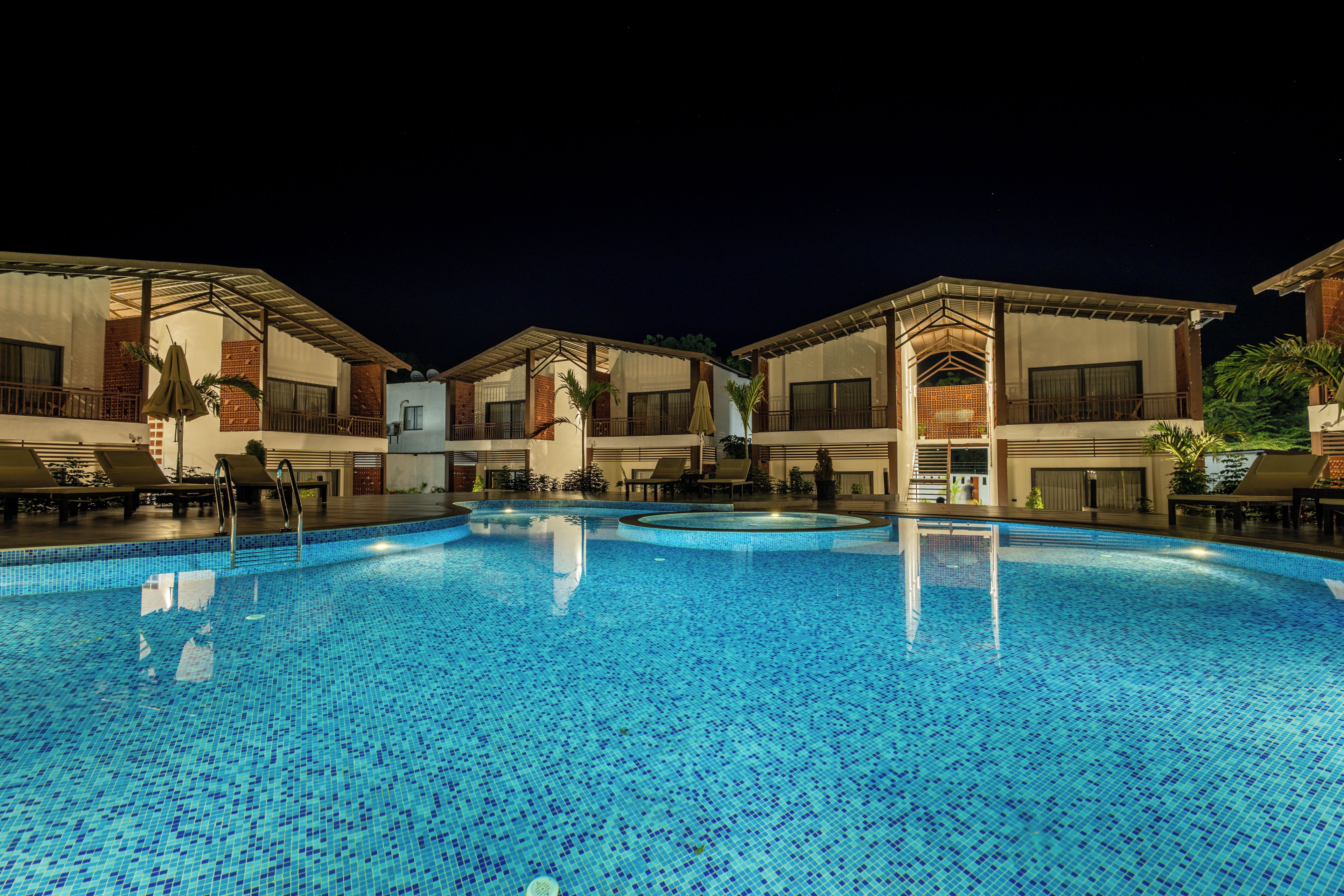 A swimming pool with a tiled surface, surrounded by buildings with balconies and outdoor seating areas.