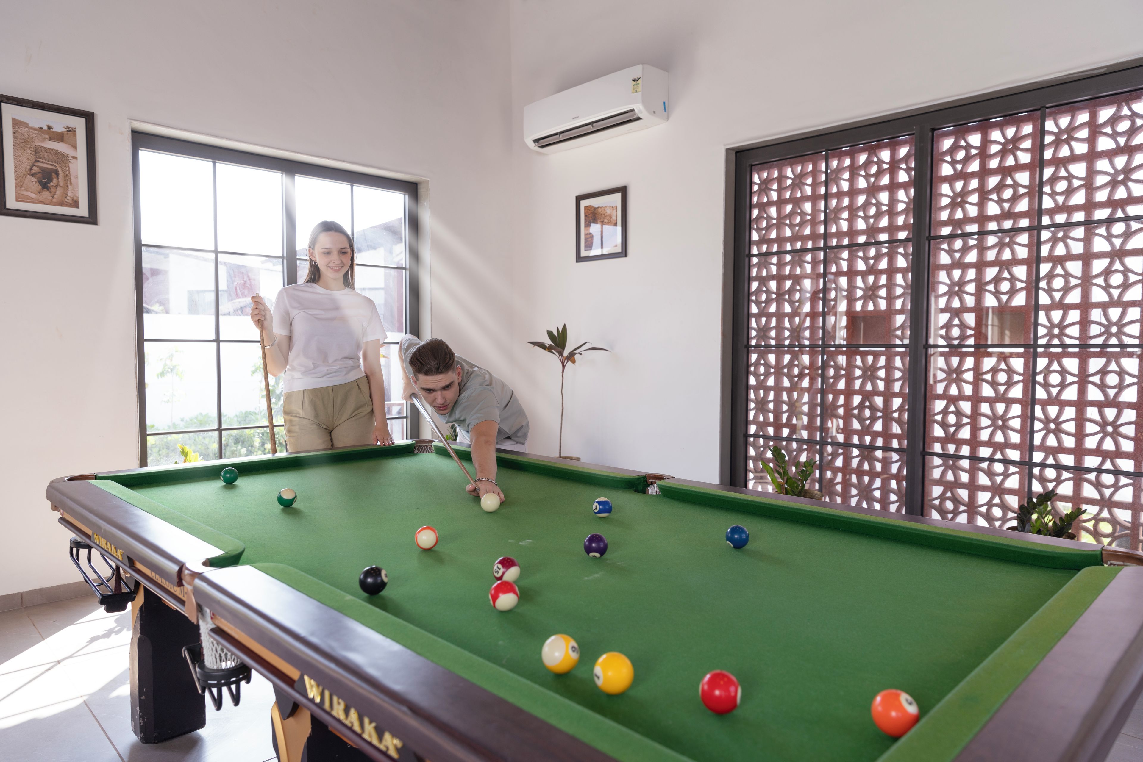 Una mesa de billar con bolas, una ventana y un separador decorativo.
