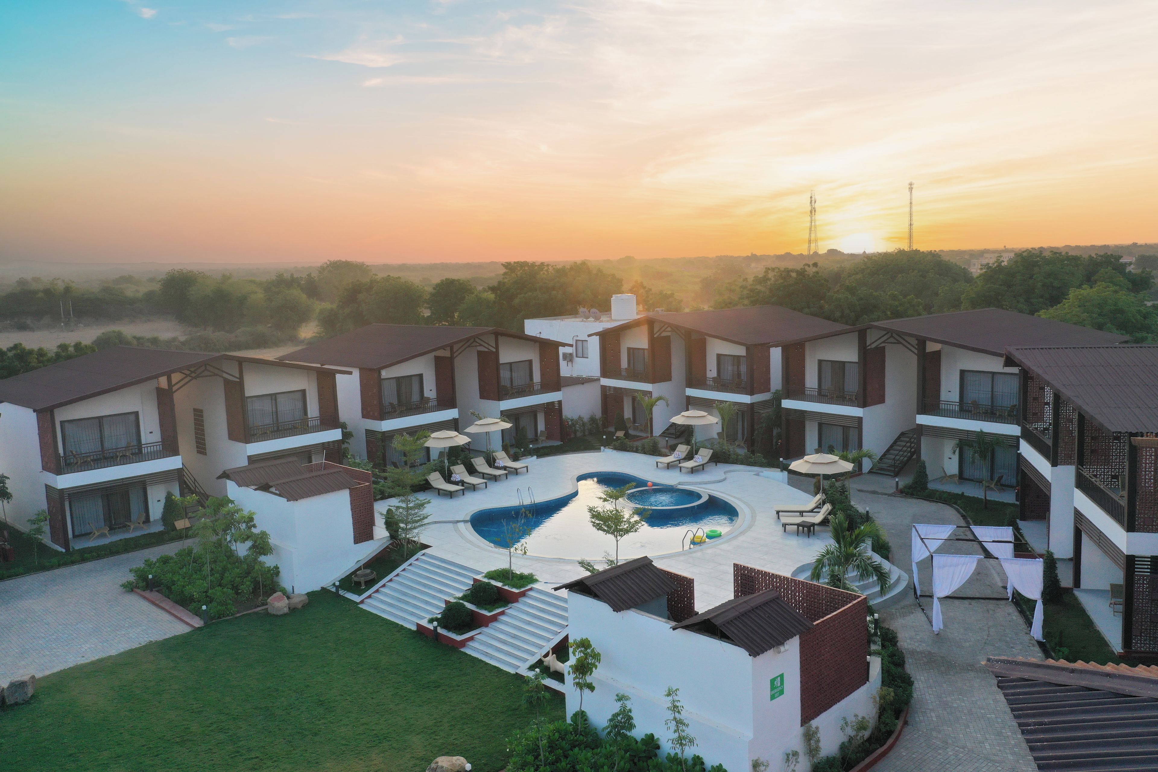 A modern hotel with a central swimming pool, multiple balconies, and a landscaped garden.