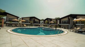 Una piscina con sillas de descanso y sombrillas, rodeada de edificios modernos con balcones.