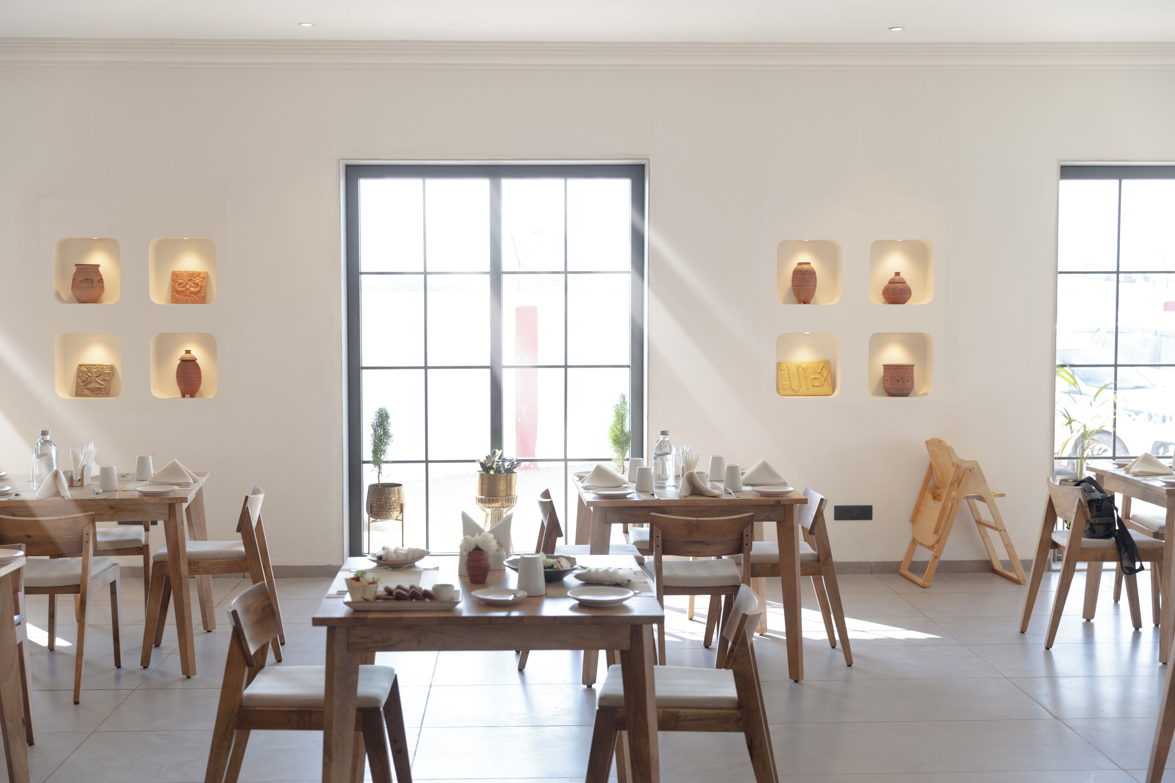 A dining area with wooden tables and chairs, a large window, and wall-mounted pottery.