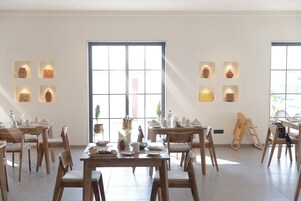 A dining area with wooden tables and chairs, a large window, and wall-mounted pottery.