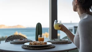 A person seated at a table with a plate of food, a glass of orange juice, and a cactus in the background. - Coocono Tinos Private Villas (Tinos)