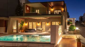 A modern two-story building with a swimming pool, outdoor seating, and warm lighting.
