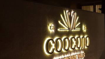A modern building with a prominent illuminated sign reading "COOCONO TINOS PRIVATE VILLAS".