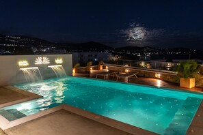 Une piscine sur le toit, agrémentée d’une cascade, avec un espace salon extérieur et une vue sur la ville la nuit.