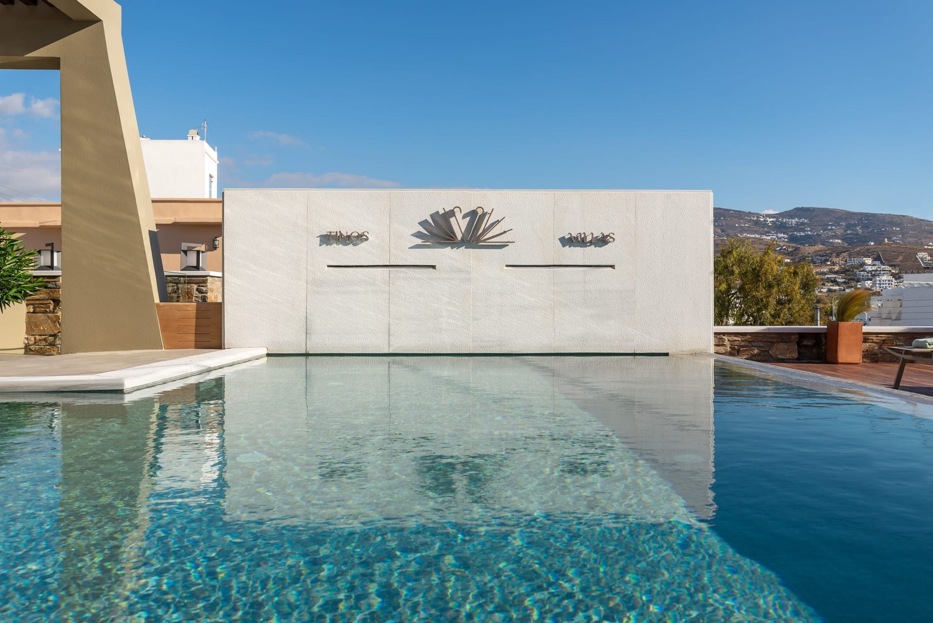 Uma piscina com água cristalina, uma parede branca com um logotipo e vista para um morro.