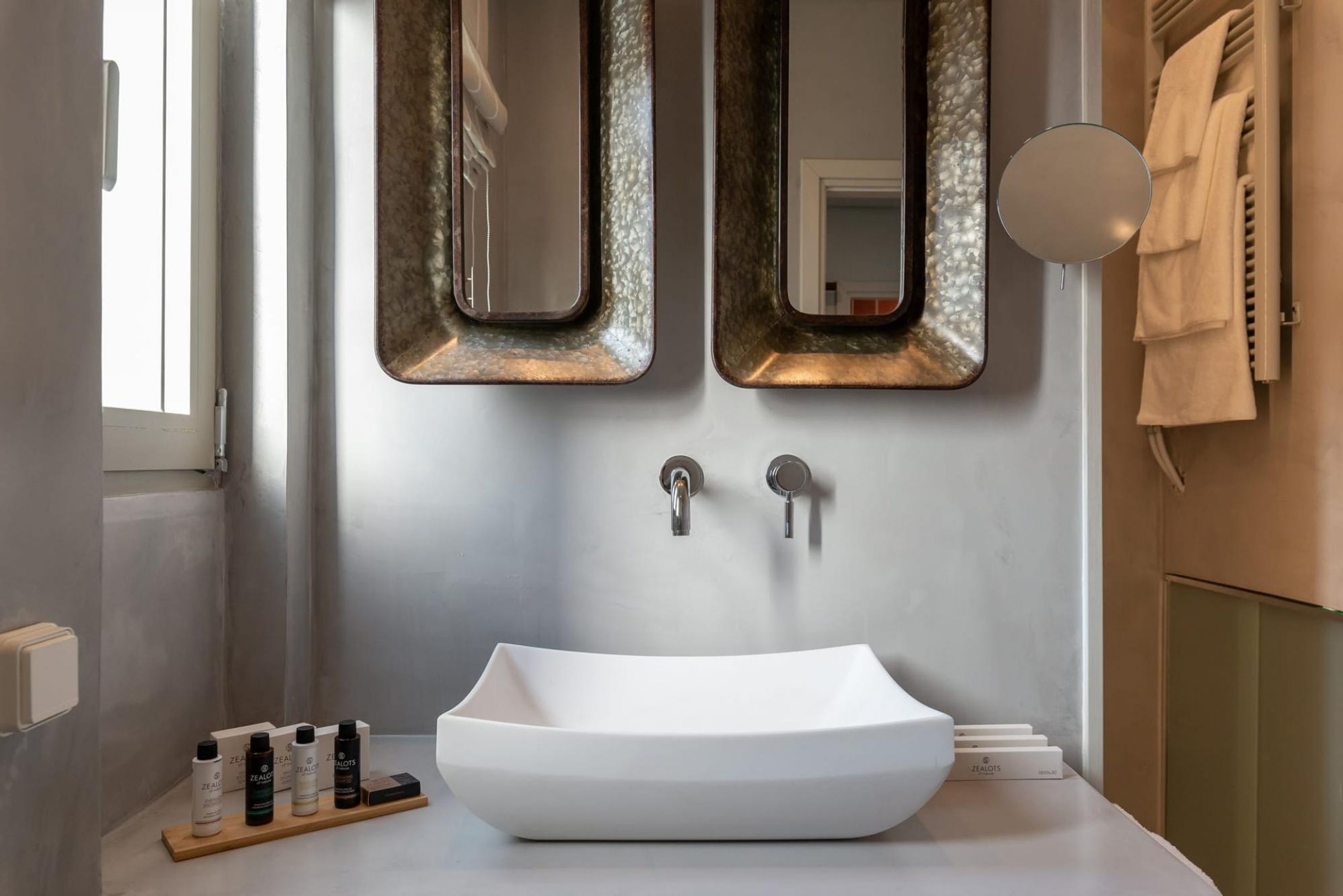 Un baño con un lavabo blanco tipo recipiente, dos espejos montados en la pared y un perchero para toallas.