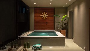 A modern spa area with a wooden wall, a glowing star-shaped light, a glass-enclosed hot tub, and a plant. - Coocono Tinos Private Villas (Tinos)