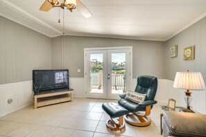 A living room with a television, a leather chair, a lamp, and a view through a glass door to an outdoor balcony. - North Fort Myers Golf Retreat w/ Patio + View! (North Fort Myers)